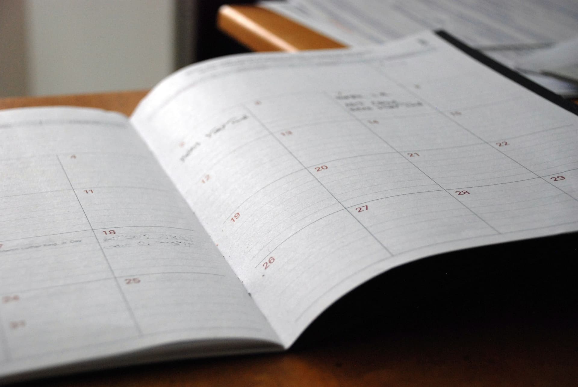 An open monthly planner with dates marked on a wooden desk