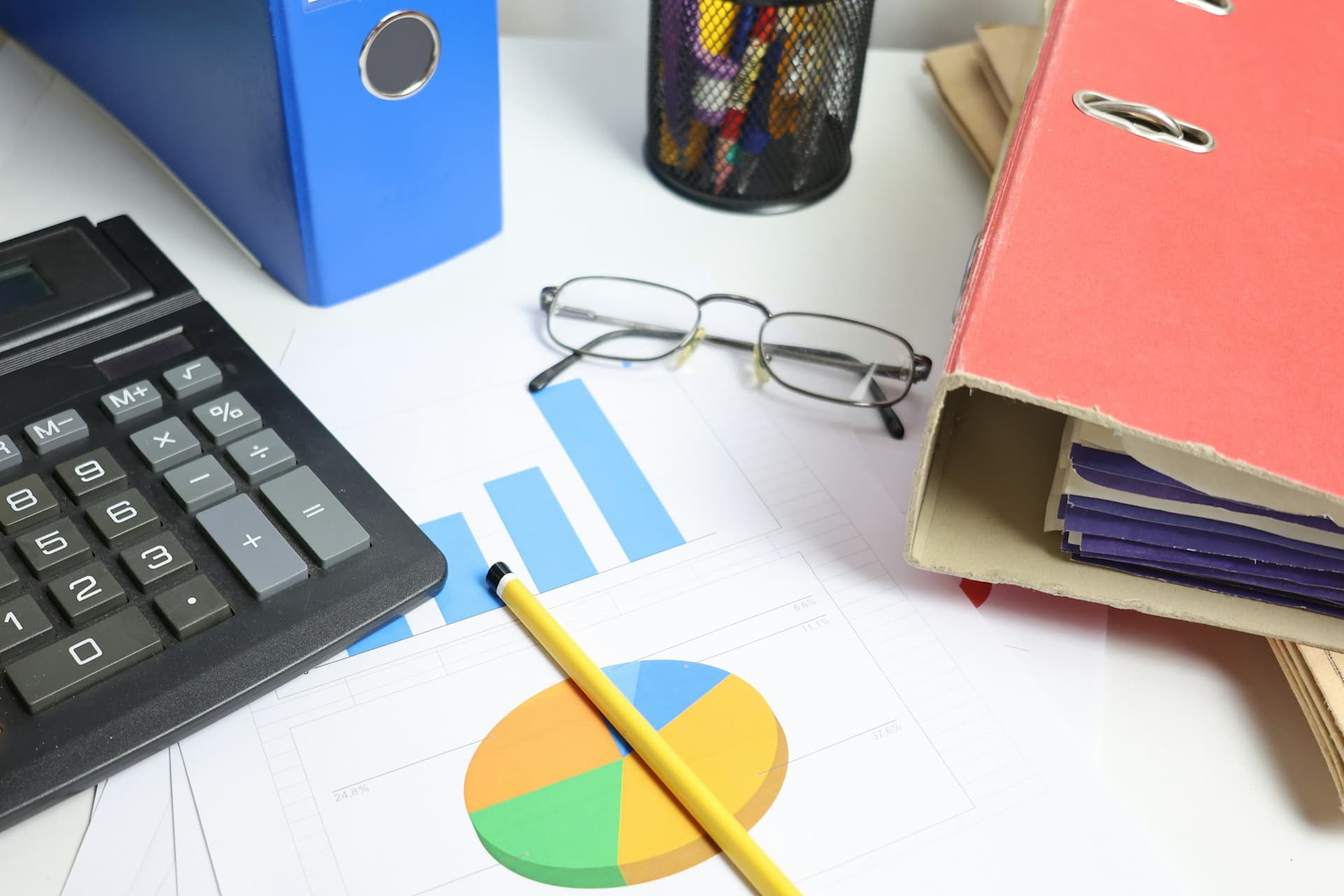 A calculator, printed charts and ring binders on an accounting desk