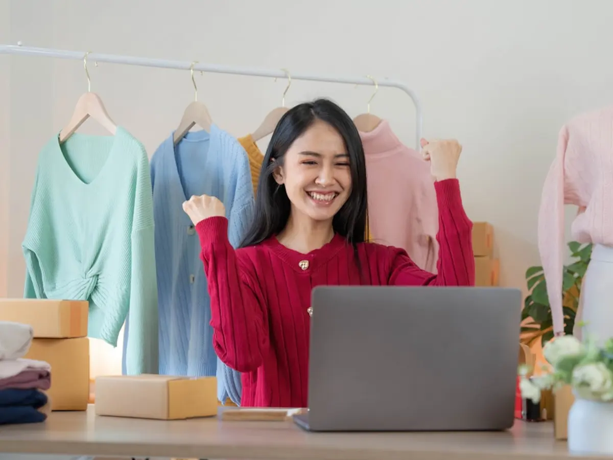 Store owner smiling at her laptop in front of a clothing rail