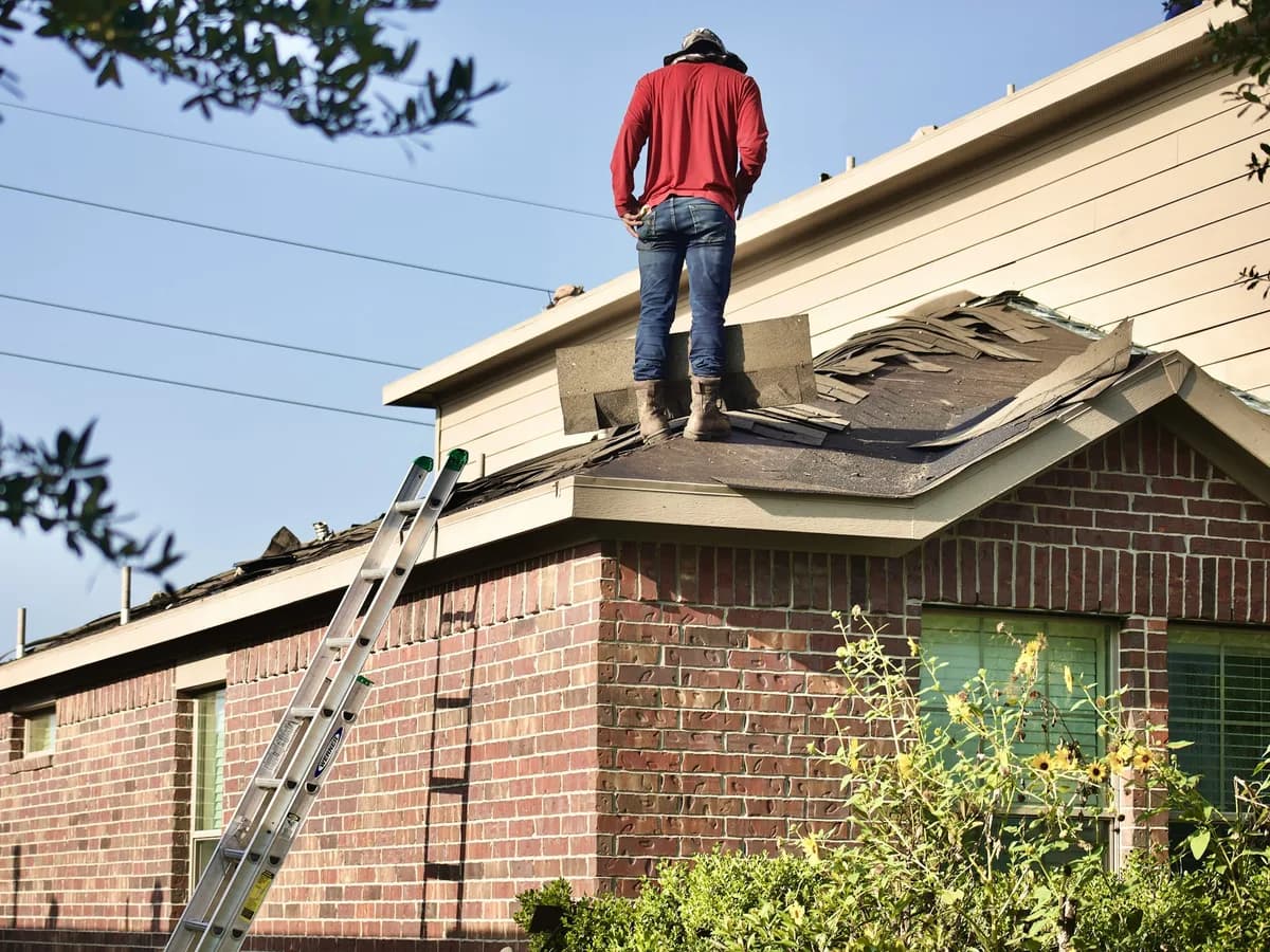Roofer standing on the roof of a brick house beside an extension ladder
