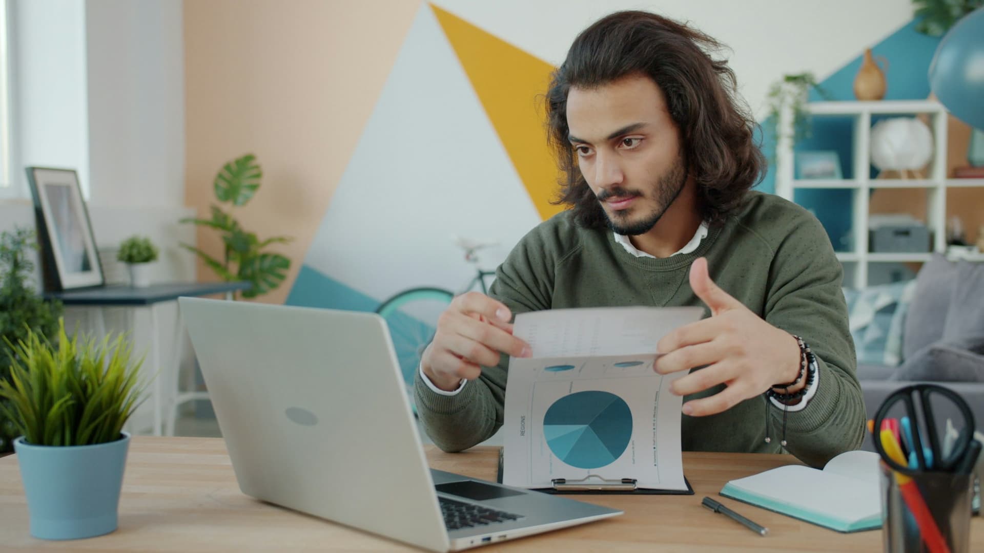 A business owner comparing a printed chart with figures on his laptop