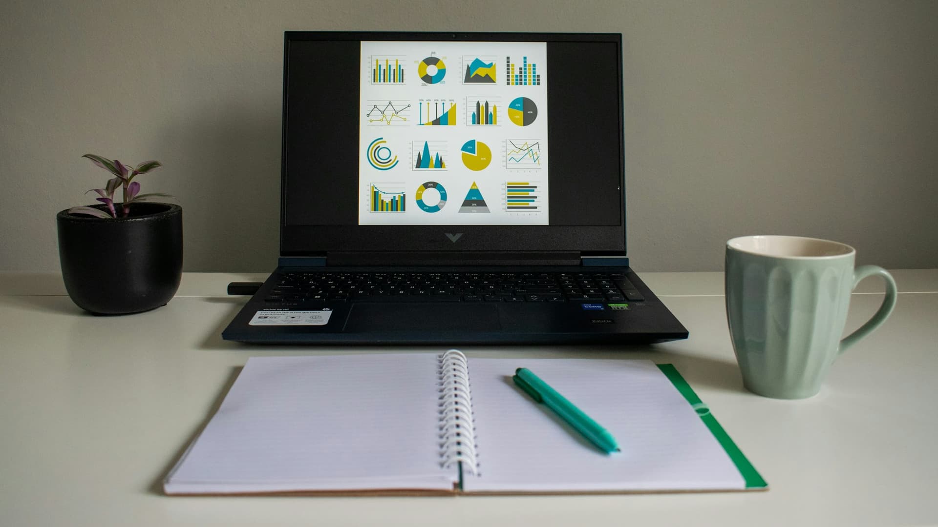 A laptop showing report charts beside an open notebook on a desk