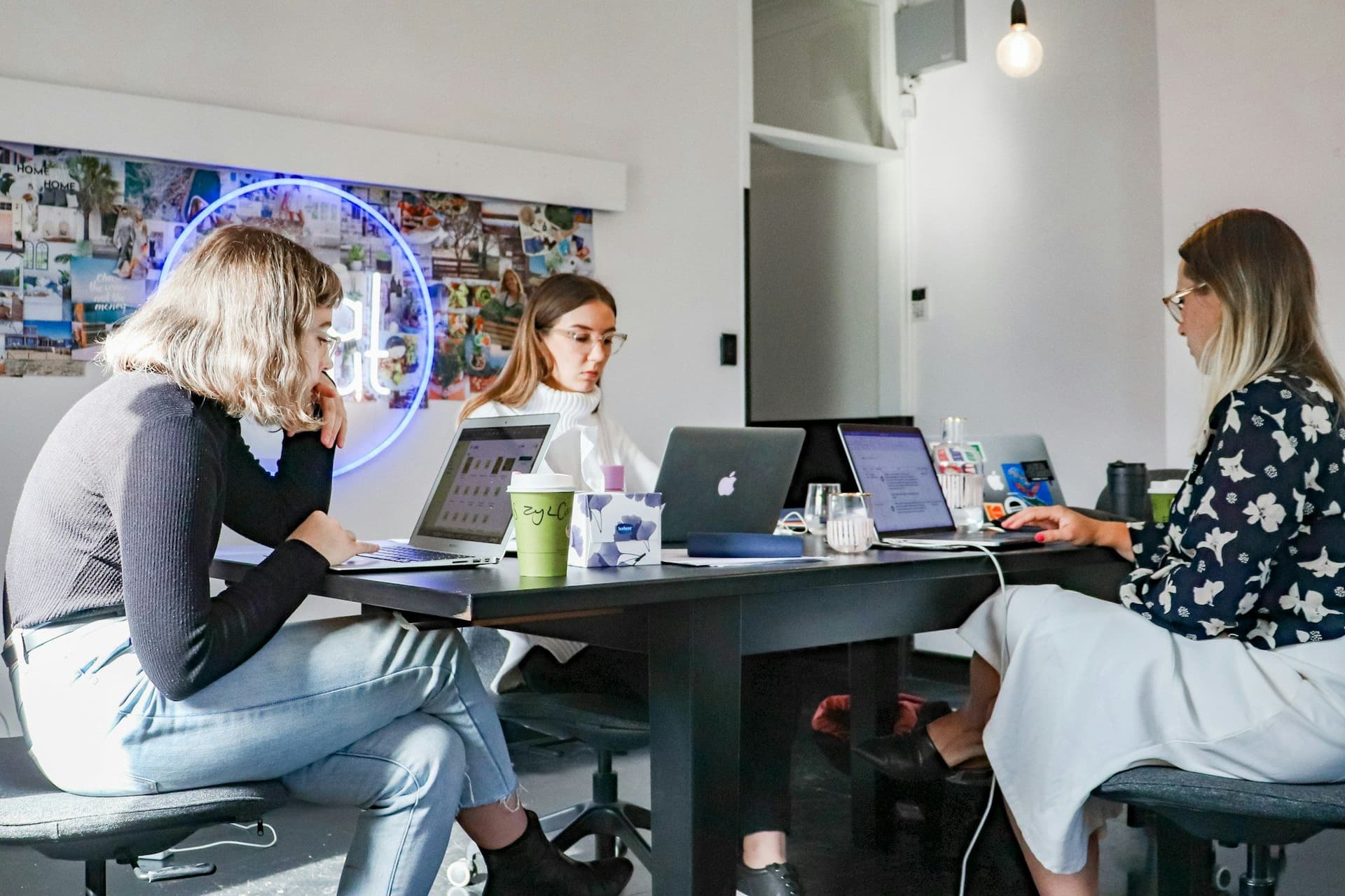 Three people working on laptops in front of an agency mood board