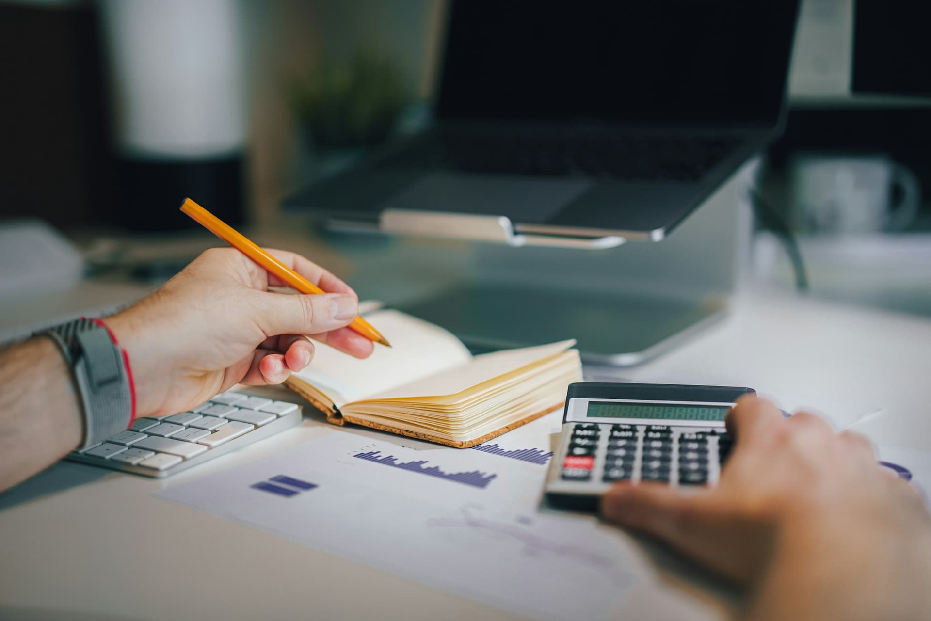 Hands checking figures with a calculator and notebook against printed reports