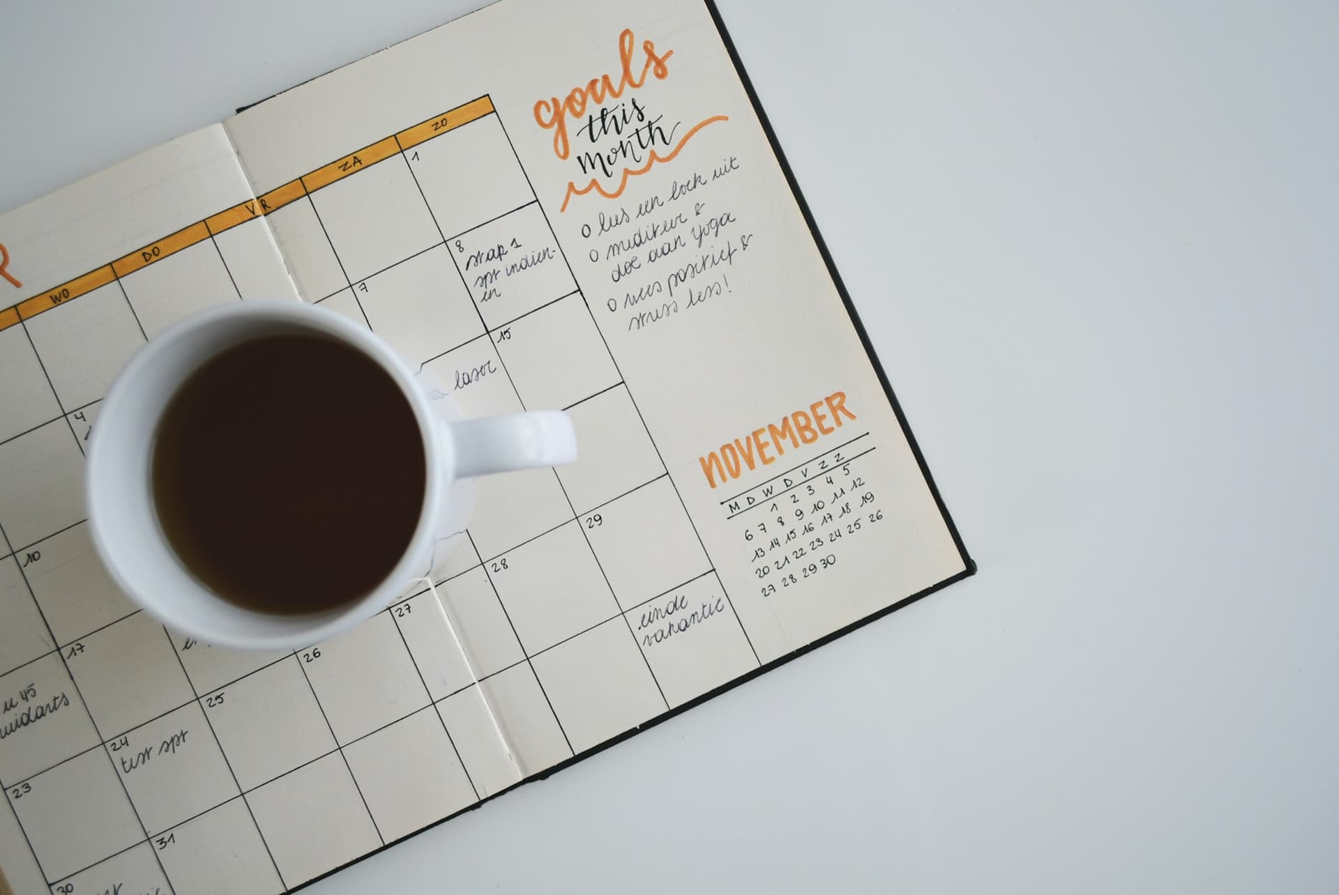A monthly planner open beside a cup of coffee, with the month's dates marked