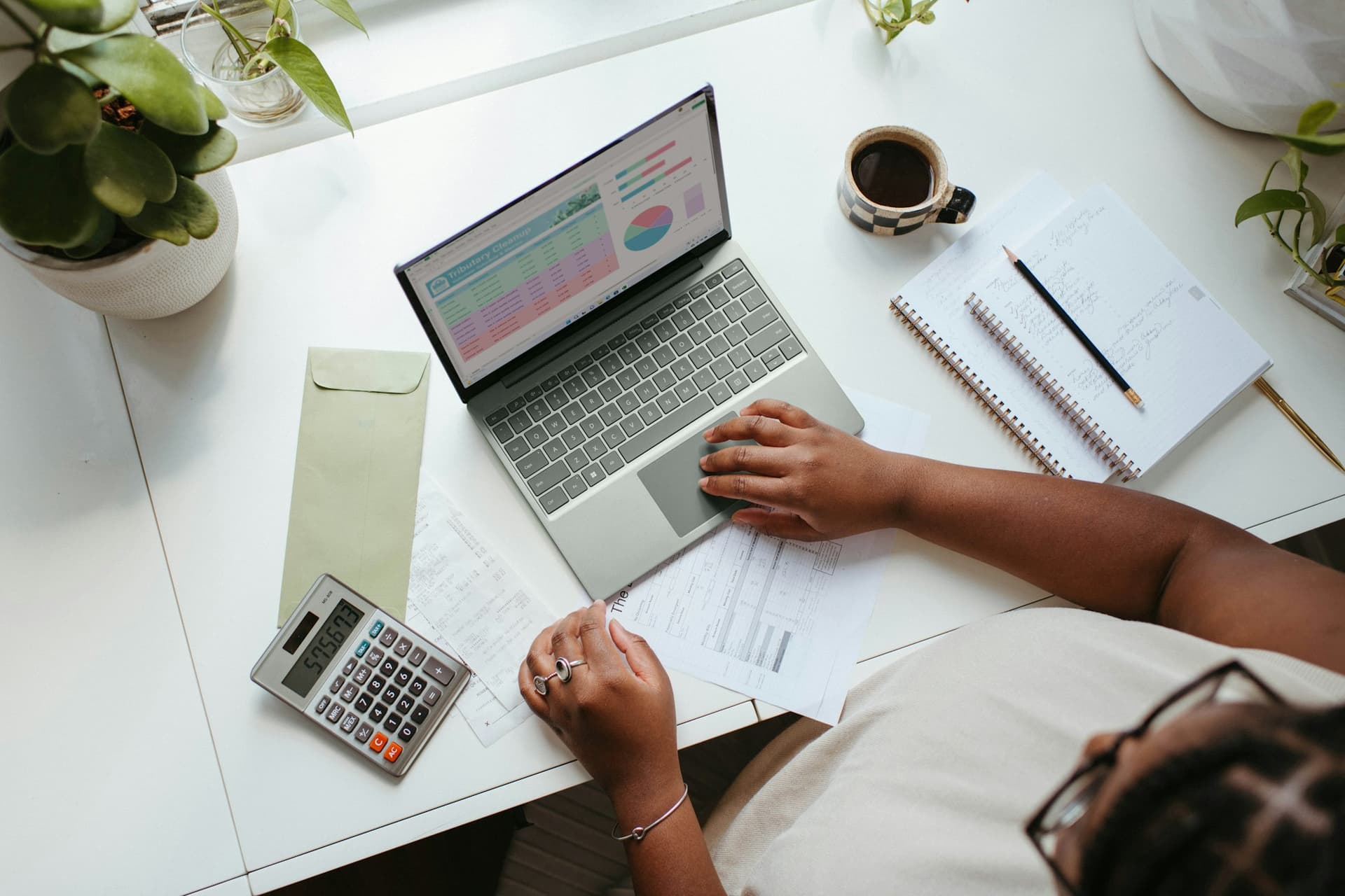 A business owner coding expenses on a laptop with receipts and a calculator on the desk