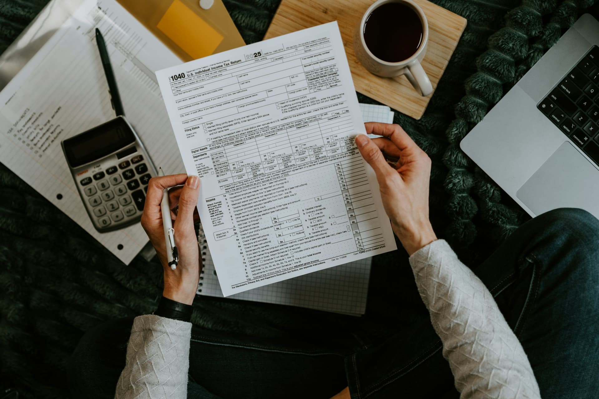 Hands holding a tax return next to a calculator, notes and a laptop